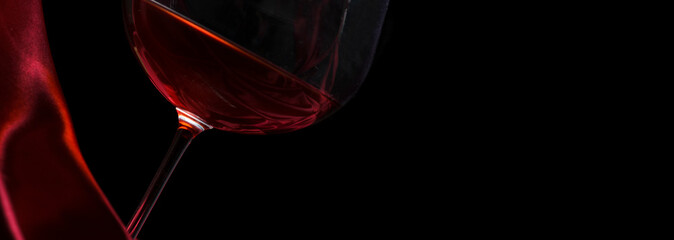 Glass of red wine on red silk against black background. Wine list design background.