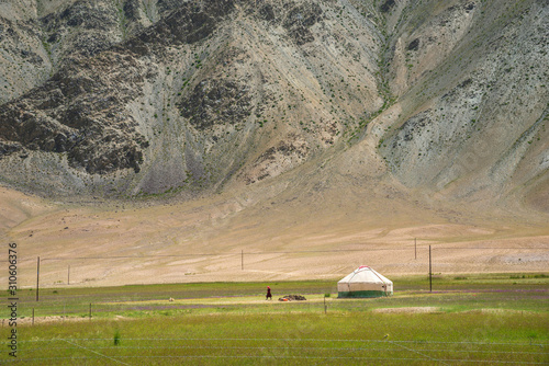White yurt and a woman on pastures at the foot of the mountain