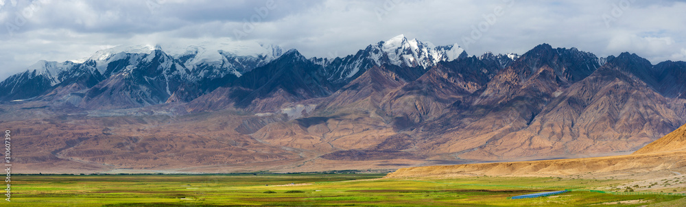 Panoramic landscape of snow-capped mountain ranges with fresh green meadows of prairie