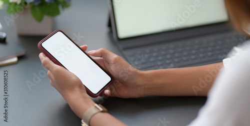 Cropped shot of young businesswoman working on her project while using smartphone in modern workplace