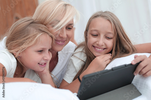 mom with her little girls watching videos lying on the bed