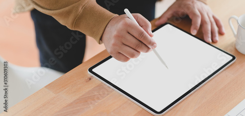 Close-up view of young man working on his project with blank screen tablet