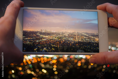 Closeup of hands taking a photo with a mobile phone from observatory down to Los Angeles at night