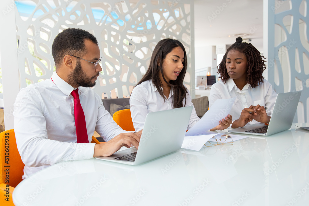 Young business people working with papers and laptop. Professional multiethnic business team working with computers and documents in office. Business and technology concept