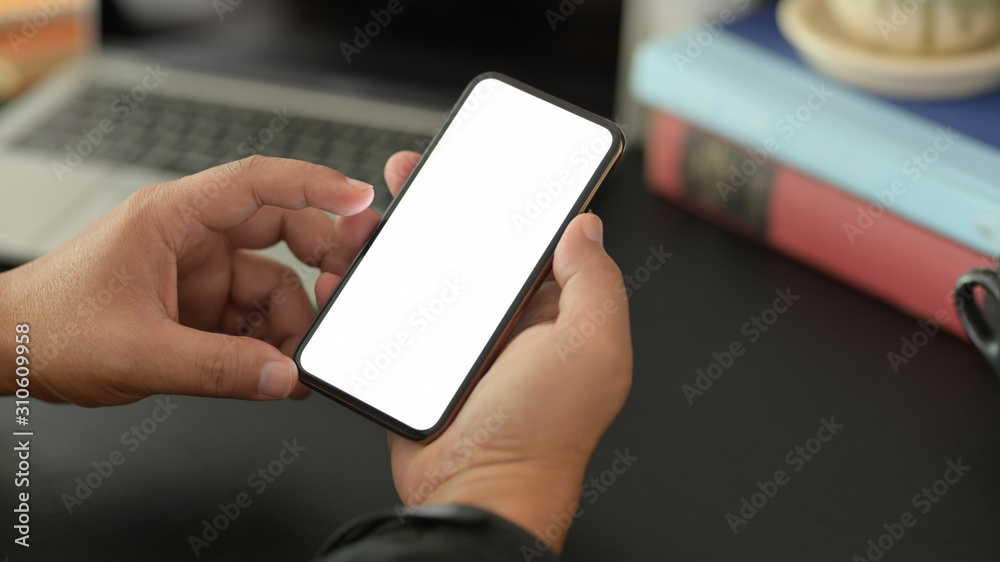 Close-up view of young businessman using blank screen smartphone in dark modern office Close-up view of young businessman using blank screen smartphone in dark modern office