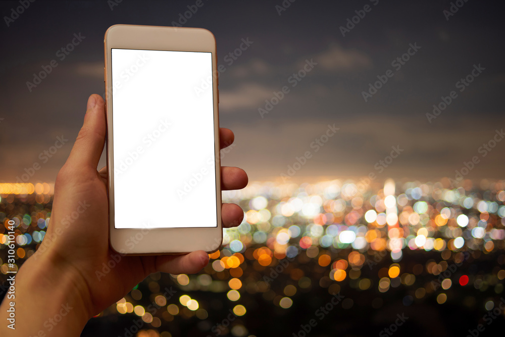 Hand holding a mobile phone with blank display, unsharp city lights in ...