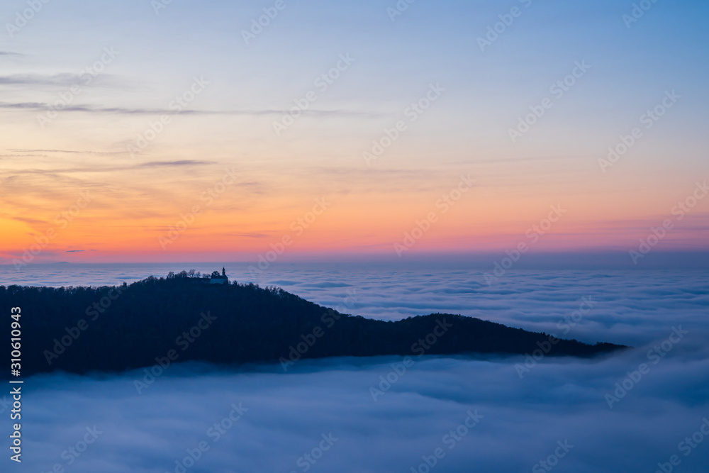 Germany, Magical aerial view above fog clouds surrounding castle teck on teckberg mountain in swabian jura nature landscape at sunset near stuttgart