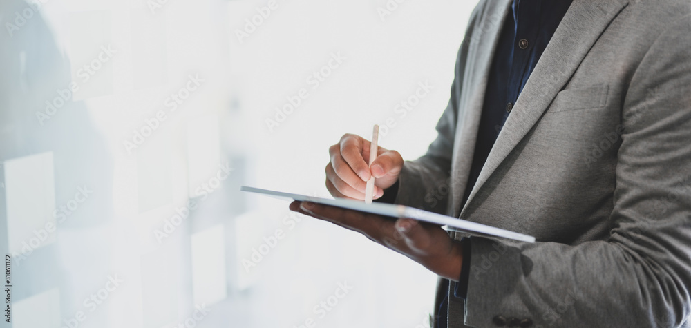 Cropped shot of young businessman using tablet while working on his project in office Cropped shot of young businessman using tablet while working on his project in office