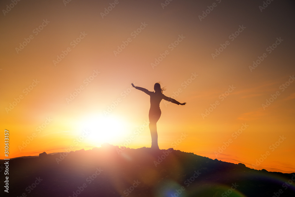 Happy girl on the top of the mountain against the sunset, success and achievement, winner. Hands up