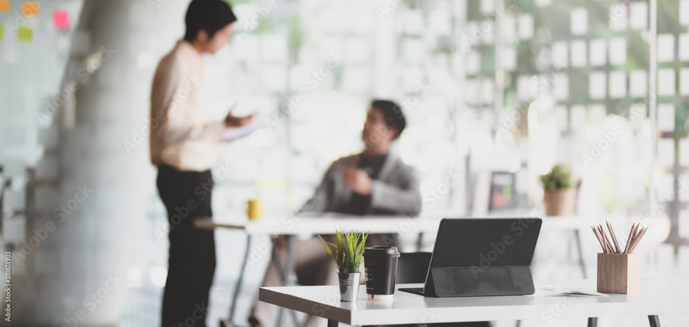 Modern office with tablet and office supplies on table with business people in the background