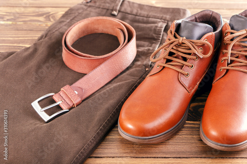 Men's leather shoes, trousers and belt on a wooden table. Modern Men's casual outfits.