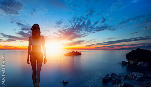 Silhouette of slim sexy girl standing on a beach with sunset © muratart