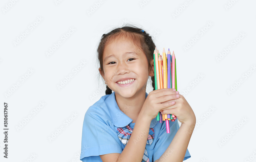 Portrait happy little girl in school uniform holding color pencils over white background. Education and school concept. Portrait happy little girl in school uniform holding color pencils over white background. Education and school concept.