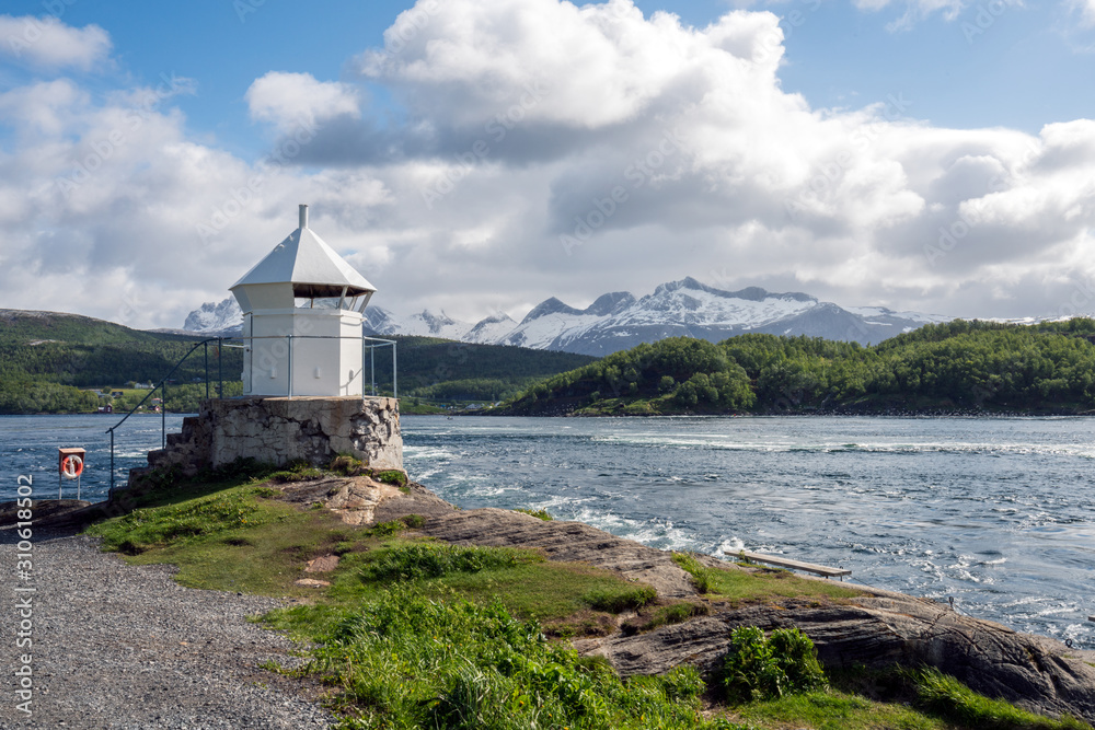 Saltstraumen river in Bodo in Northern Norway. Snow covered mountains in the background and blue cloudy sky, lighthouse in the foreground. Traveling and holiday concept.