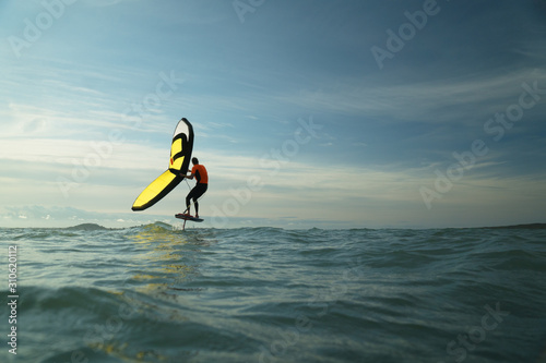 Canvas Print Man riding a hydrofoil surfboard using a hand held inflatable foil wing