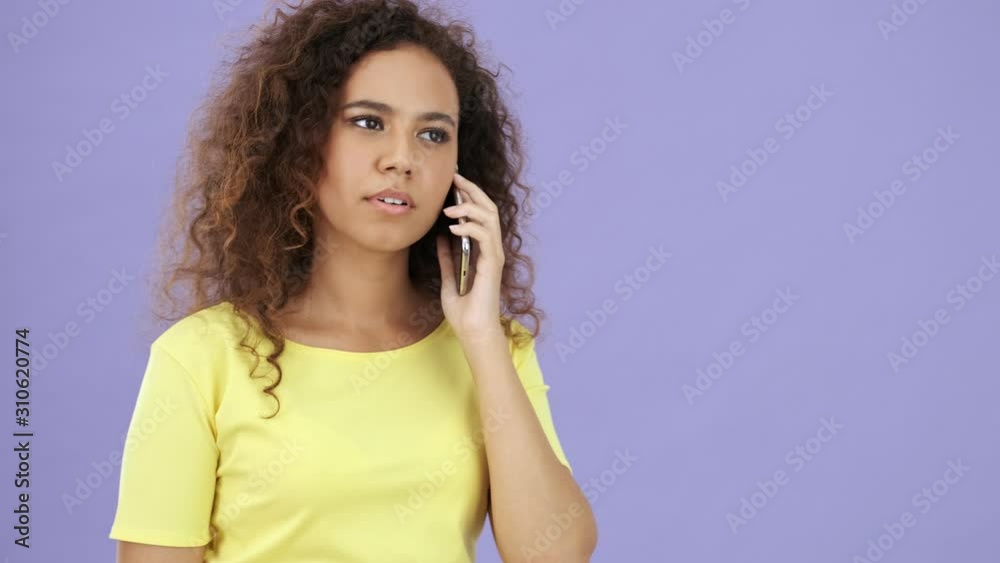 African young woman in yellow t-shirt having an annoying call while looking at the camera over purple background isolated 