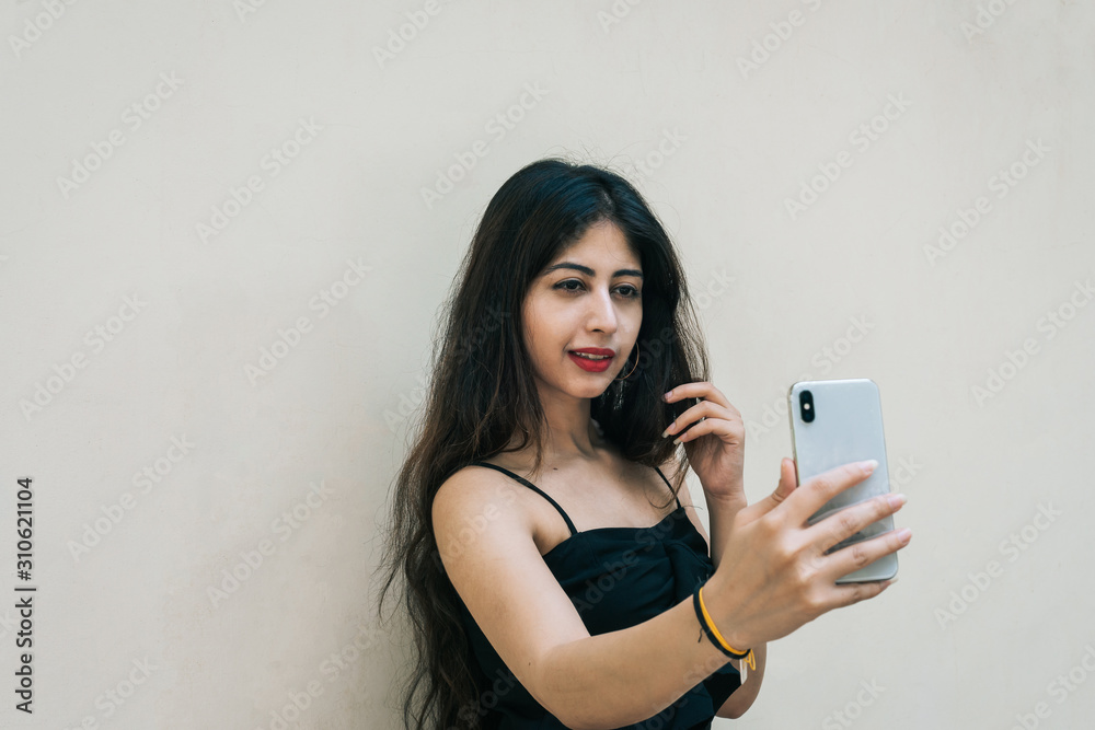 Naklejka premium One Indian female outdoor taking selfie with smart mobile phone on isolated background