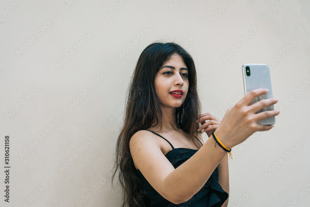 One Indian female outdoor taking selfie with smart mobile phone on isolated background One Indian female outdoor taking selfie with smart mobile phone on isolated background