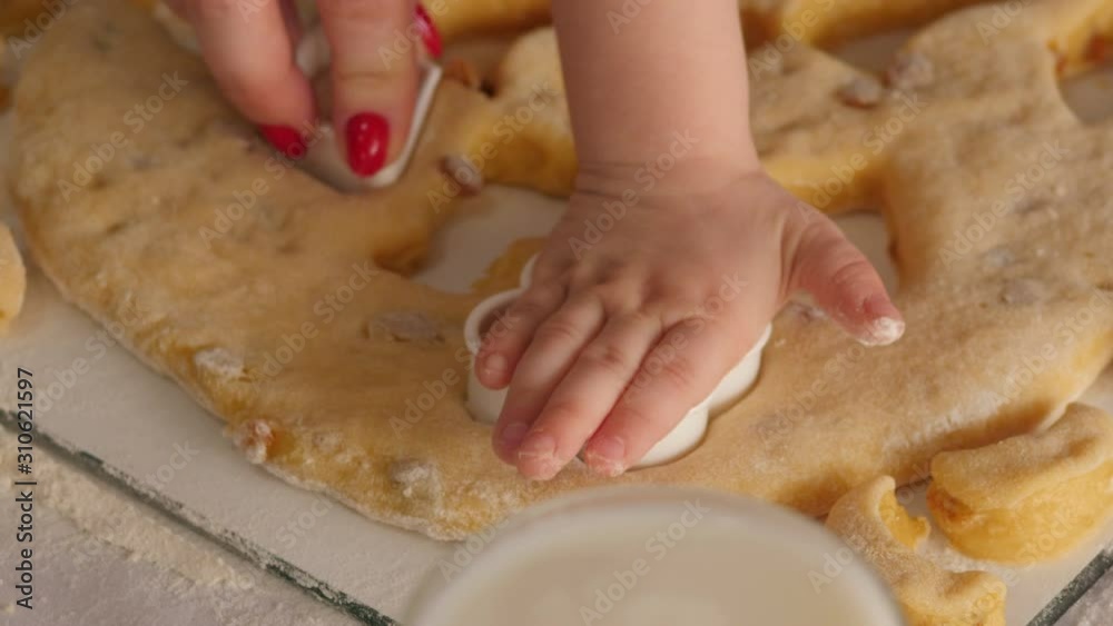 Close-up of a cute little girl with her mom cutting out different cookie shapes at home on the kitchen table. The child helps the mother to prepare sweet cookies. Close-up of a cute little girl with her mom cutting out different cookie shapes at home on the kitchen table. The child helps the mother to prepare sweet cookies.