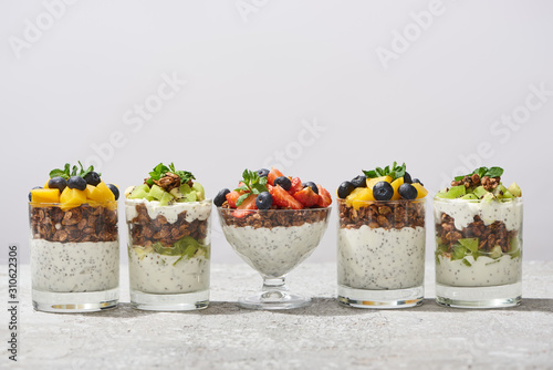 delicious granola in glasses with fruits and berries on grey concrete surface isolated on white