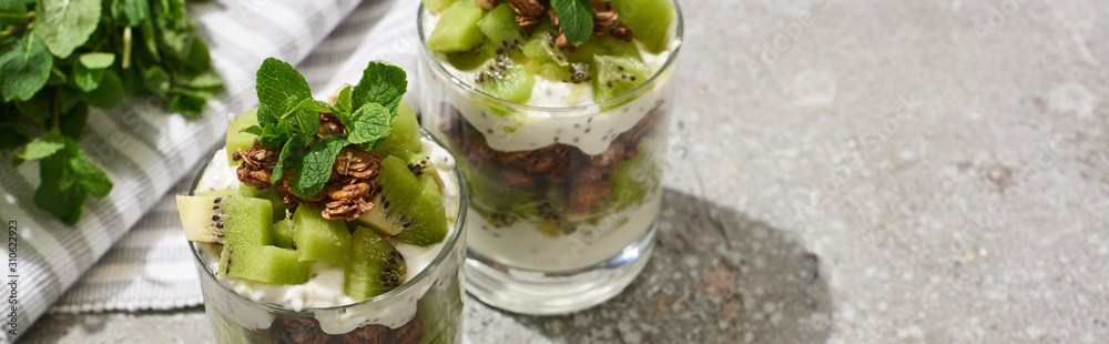 fresh granola with kiwi and yogurt on grey concrete surface with striped napkin and mint, panoramic shot fresh granola with kiwi and yogurt on grey concrete surface with striped napkin and mint, panoramic shot