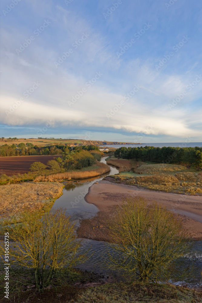 The Lunan River gently winding itself through the hills and farmland behind Lunan Bay on the east coast of Scotland in December.