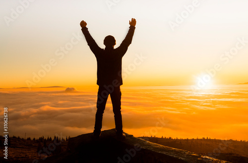 Silhouette of success and serenity young man standing on a rock in the mountains at sunset. 