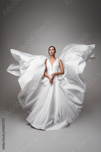Pretty dark-haired girl in a flying wedding dress. White dress fluttering in the wind. Fashion Wedding Photography Concept