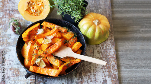 Baked pumpkin slices in a pan with herbs and garlic. Autumn lunch. Vegan food. Healthy snack.