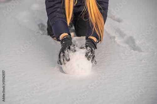 Fototapeta Young woman rolling giant snowball to make snowman