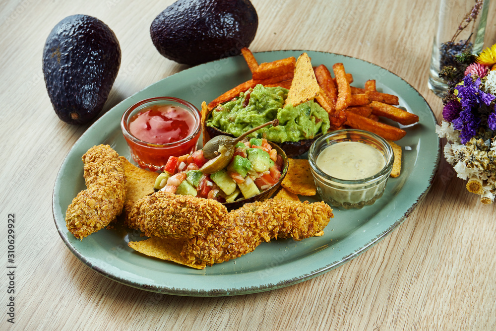 Set of avocado appetizers. Deep fried avocado sticks in crispy breading. Guacamole and nachos. Stuffed avocado with capers and tomatoes. Sweet potato with sauces on a plate. Great lunch