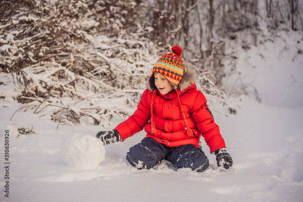 Cute boy in red winter clothes builds a snowman. Winter Fun Outdoor Concept