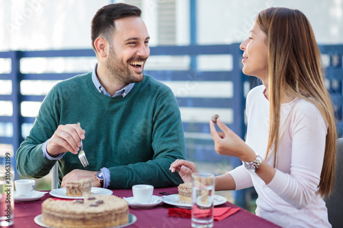 Beautiful smiling happy young couple eating cake and drinking coffee after lunch in a restaurant. Celebrating birthday or relationship anniversary