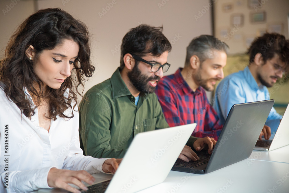 Focused coworkers using laptops at meeting table. Business colleagues in casual working together in contemporary office space. Communication concept Focused coworkers using laptops at meeting table. Business colleagues in casual working together in contemporary office space. Communication concept