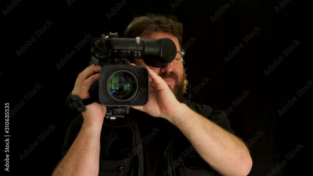Concept idea: Bearded TV cameraman with professional broadcast video camera on black background Concept idea: Bearded TV cameraman with professional broadcast video camera on black background