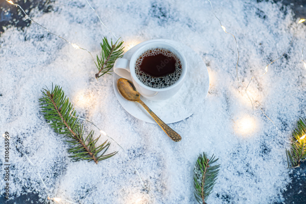 White cup with hot coffee. Stands in artificial snow. Near a branch of spruce. New Year's and Christmas.