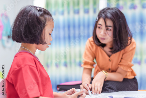 The Asian elementary school children are studying in the classroom with an Asian female teacher.