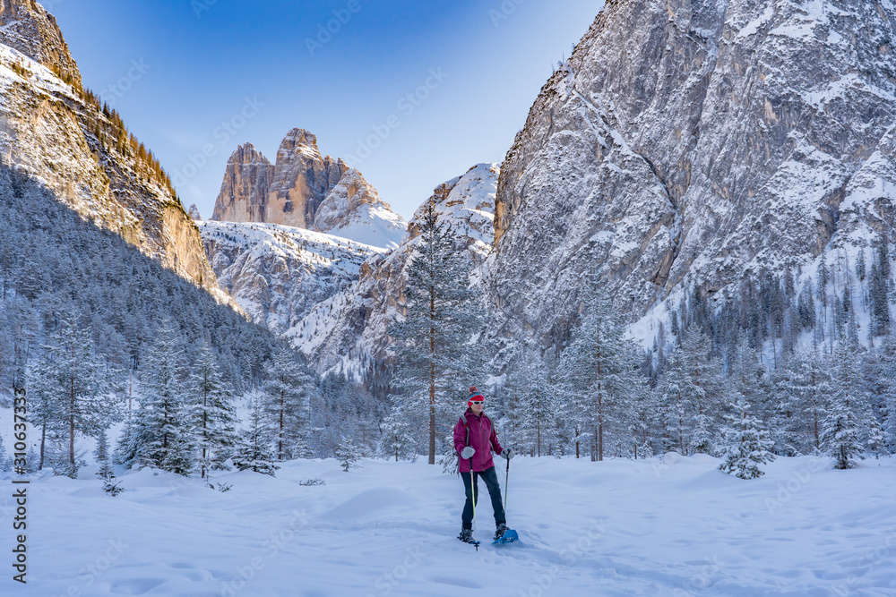 active senior woman snowshoeing in  spectacular Hoehlenstein Valley under the famous Three Peaks, Dolomites  near village of Toblach, South Tyrol, Italy