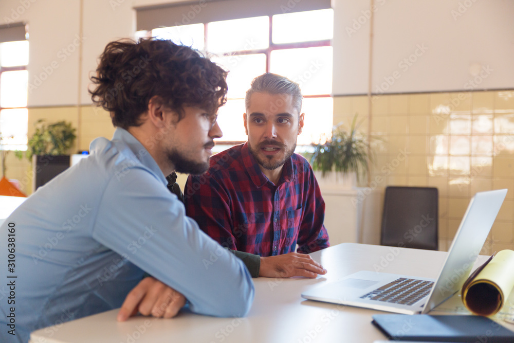Male coworkers watching content on monitor and discussing project. Business colleagues in casual working together in contemporary office space. Teamwork concept Male coworkers watching content on monitor and discussing project. Business colleagues in casual working together in contemporary office space. Teamwork concept