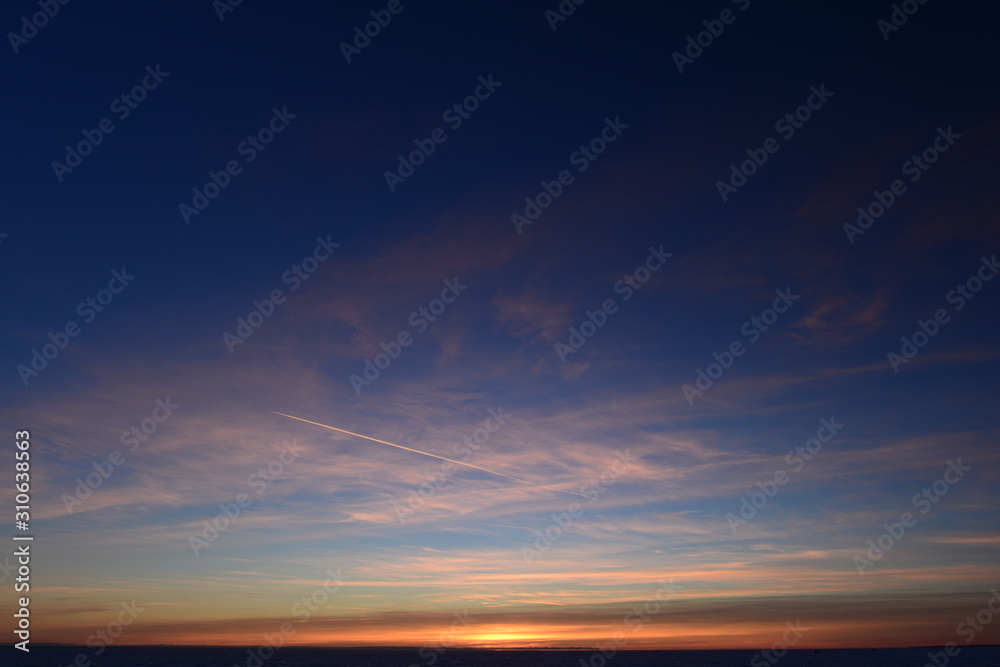 Airplane trail in the blue sky in white cirrus clouds in winter at sunset