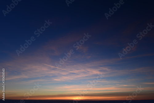 Airplane trail in the blue sky in white cirrus clouds in winter at sunset