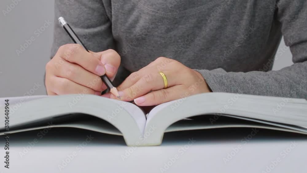 Close up of Woman's hand drawing a line and writing short summary while reading a book at library. Close up of Woman's hand drawing a line and writing short summary while reading a book at library.