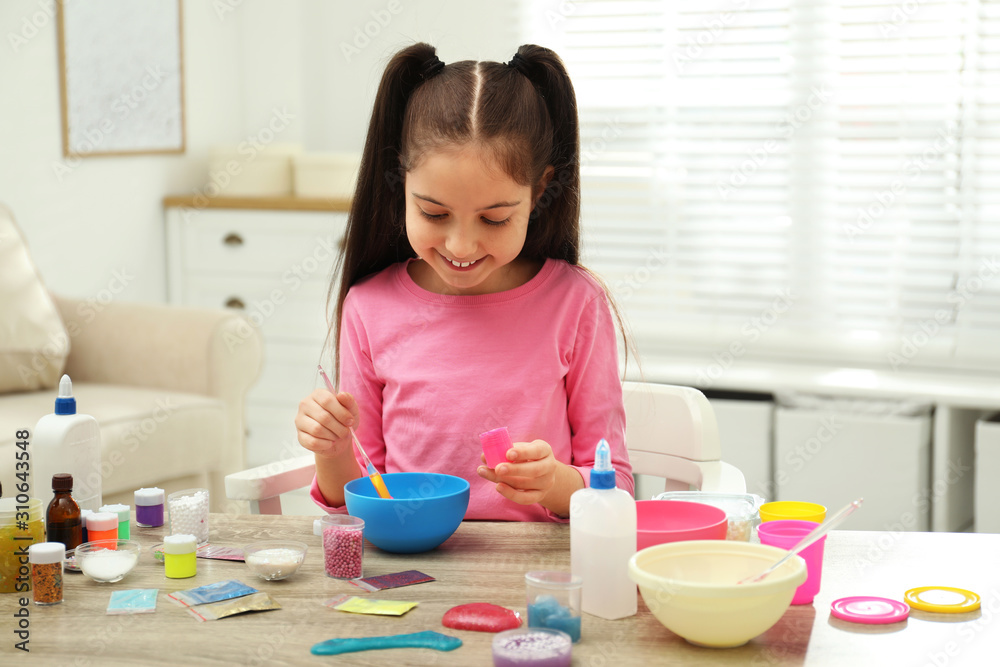 Cute little girl mixing ingredients with silicone spatula at table. DIY slime toy