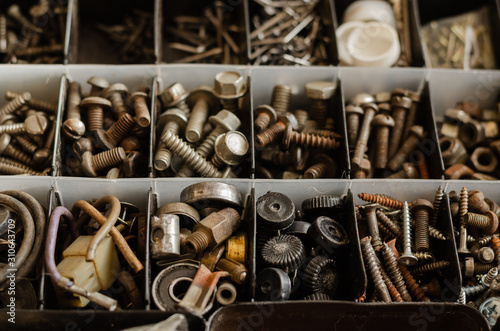 Used and new Bolts, nuts, grovers, bearings. Compartments of a plastic box with various fasteners and fittings. View from above. Selective focus. photo
