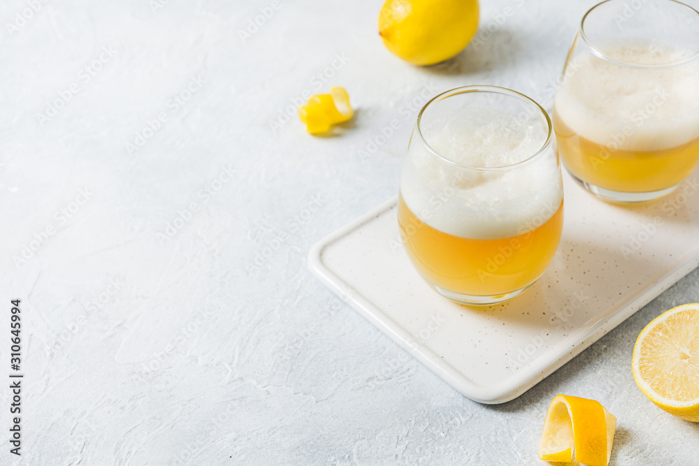 Two whiskey sour cocktails with ingredients, lemon juice, sugar syrup and egg white in glass on white. Horizontal orientation. Two whiskey sour cocktails with ingredients, lemon juice, sugar syrup and egg white in glass on white. Horizontal orientation.