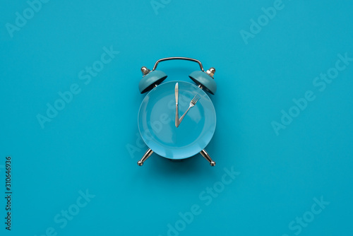 Time to eat. Plate with cutlery as clock on blue background. Top view. Flat lay. Weight loss and diet concept