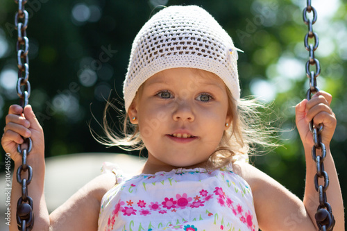 Smiling happy little girl swinging in summer park