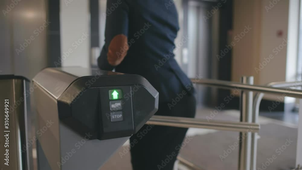 Businesswoman pass the electronic turnstile with plastic card entering modern office business center. Lady in formal clothes use card to access control