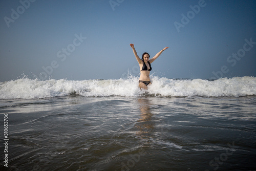 A young woman in a black swimsuit spends time in the sea or ocean. The girl takes refuge from the waves.