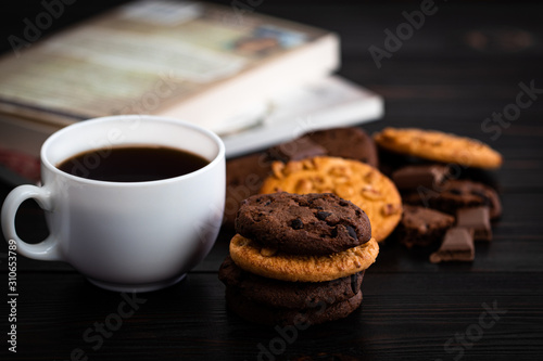 Chocolate cookies cup of coffee and book on wooden table. Homemade food on wooden background